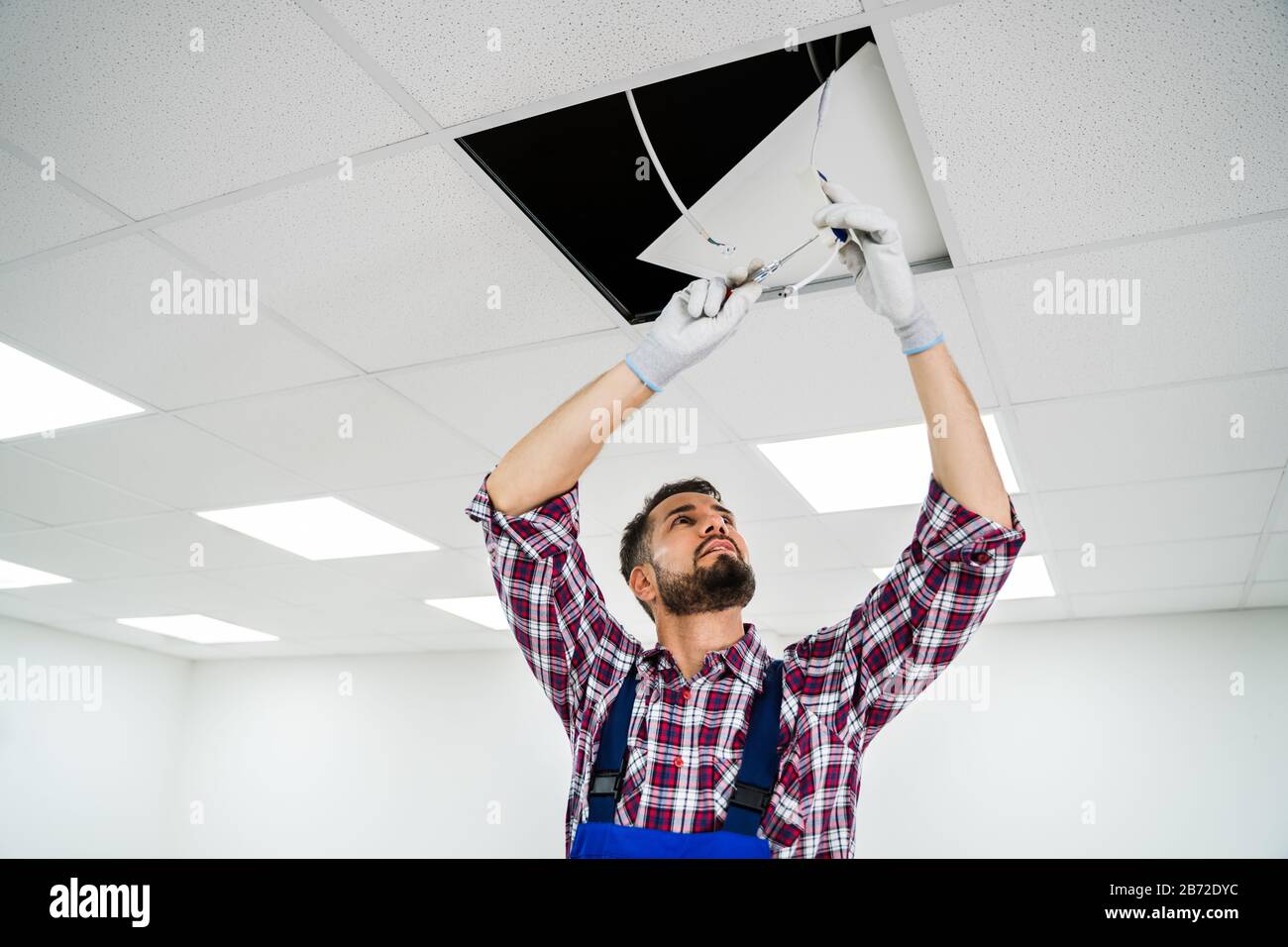 Full Length Portrait Of Electrician On Stepladder Installs Lighting To The Ceiling In Office Stock Photo