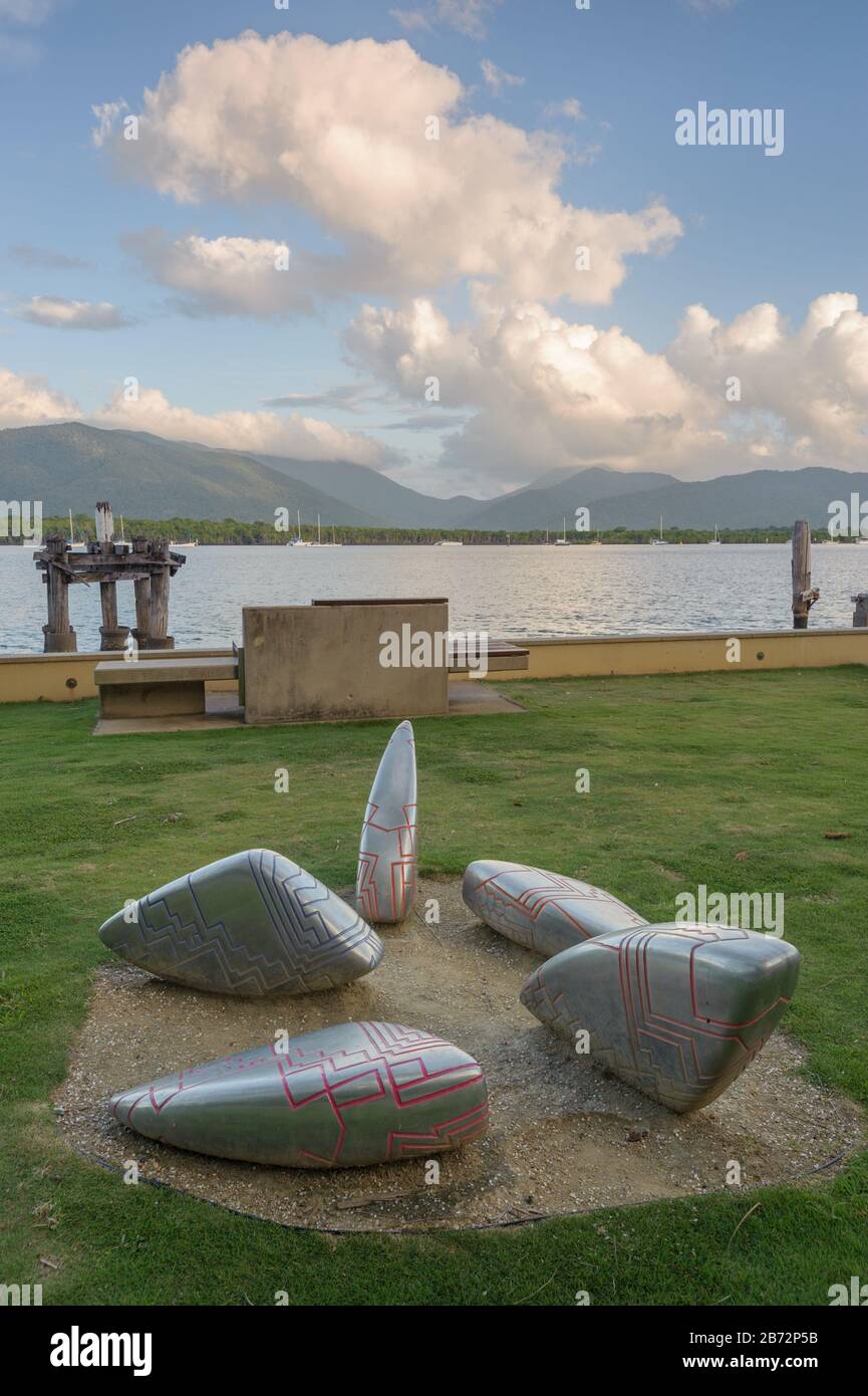 View of grassed, esplanade foreshore near Cairns wharf at Trinity Inlet with foreground art installation backed by the mangrove lined Yarrabah Range. Stock Photo