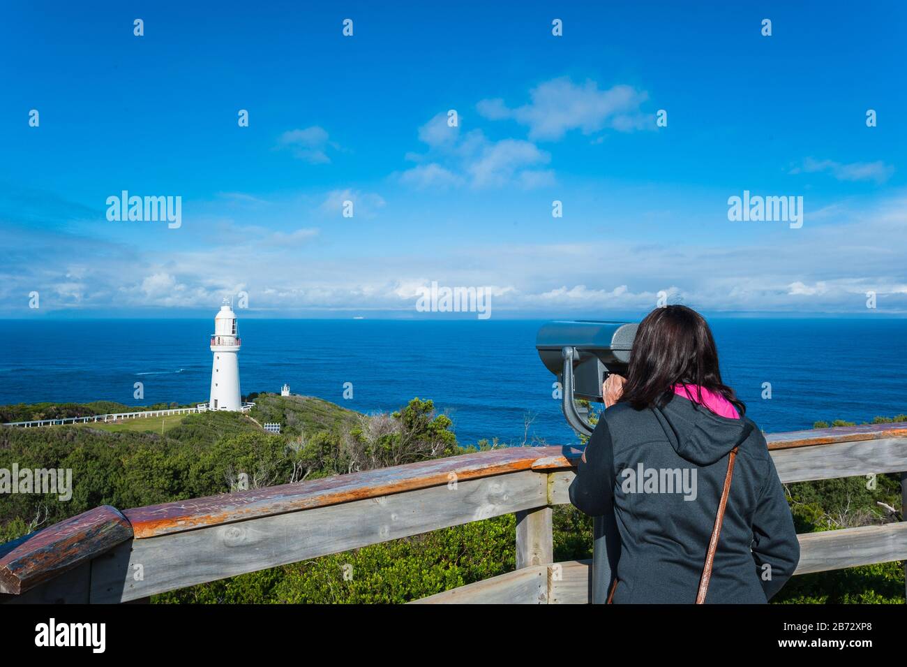 View of Cape Otway Lighthouse in Victoria, Australia as a female tourist enjoys the spectacular scene of the Southern Ocean behind the guard rails Stock Photo