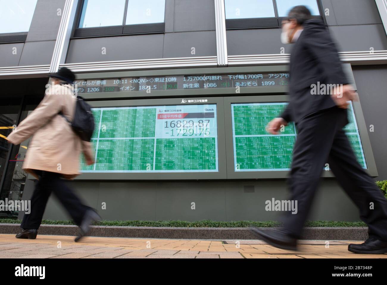 Tokyo, Japan. 13th March, 2020-. People walk past an electronic stock board  showing Japan's Nikkei Stock Average in Tokyo, Japan on March 13, 2020.  Japanese stocks plunged more than 10% during the