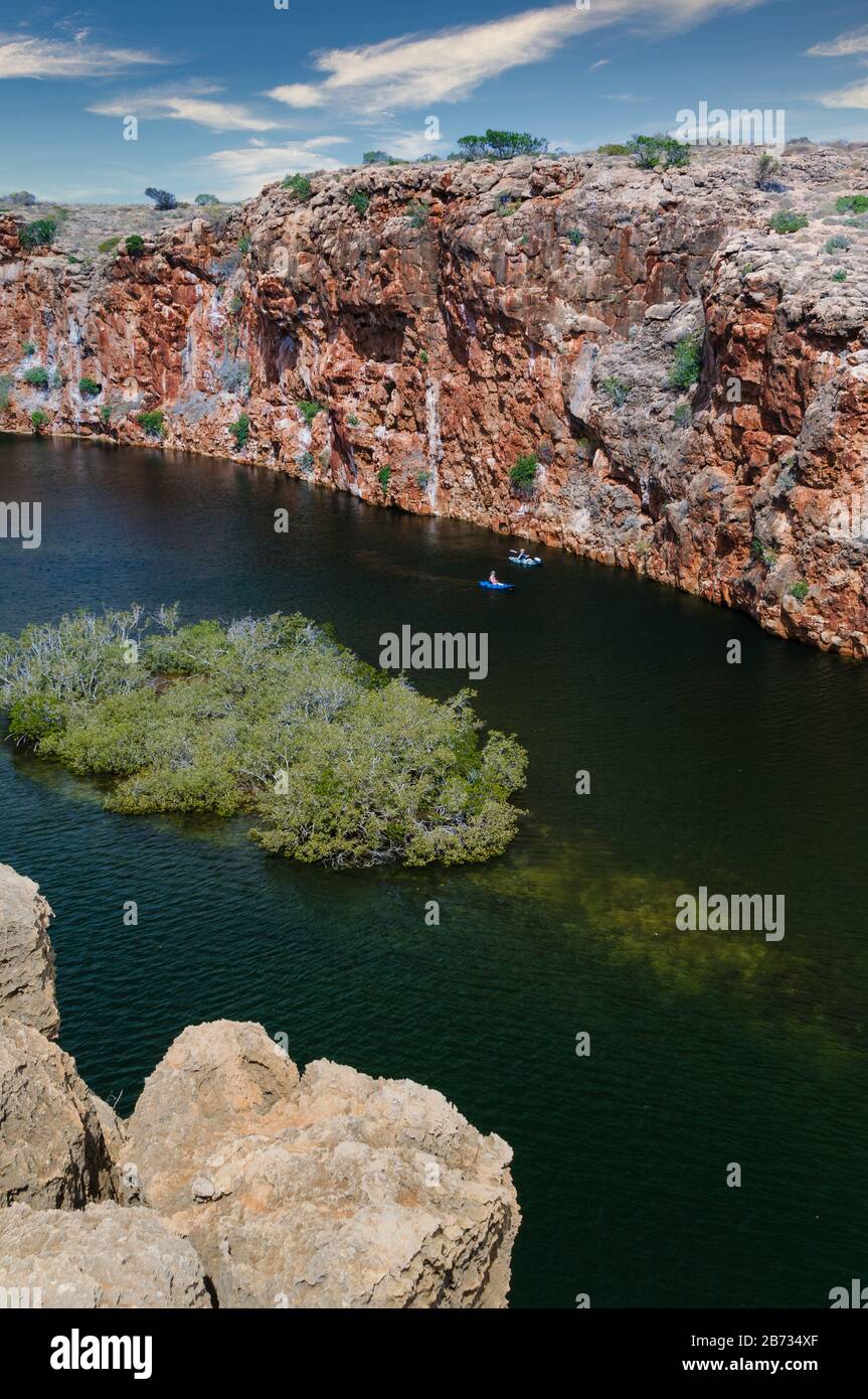 View from cliff edge down on Western Australia's Yardie Creek Gorge and cliff face, with two adventure ski paddlers navigating the creek. Stock Photo