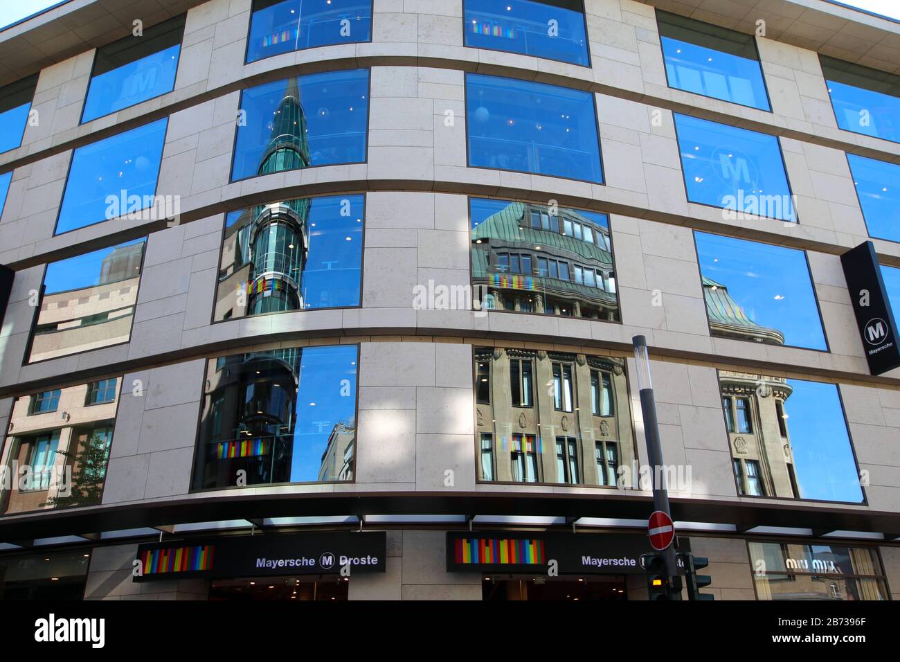 The modern glass facade of 'Mayersche Buchhandlung' in downtown Düsseldorf. The opposite buildings and the blue sky are reflecting in the facade. Stock Photo
