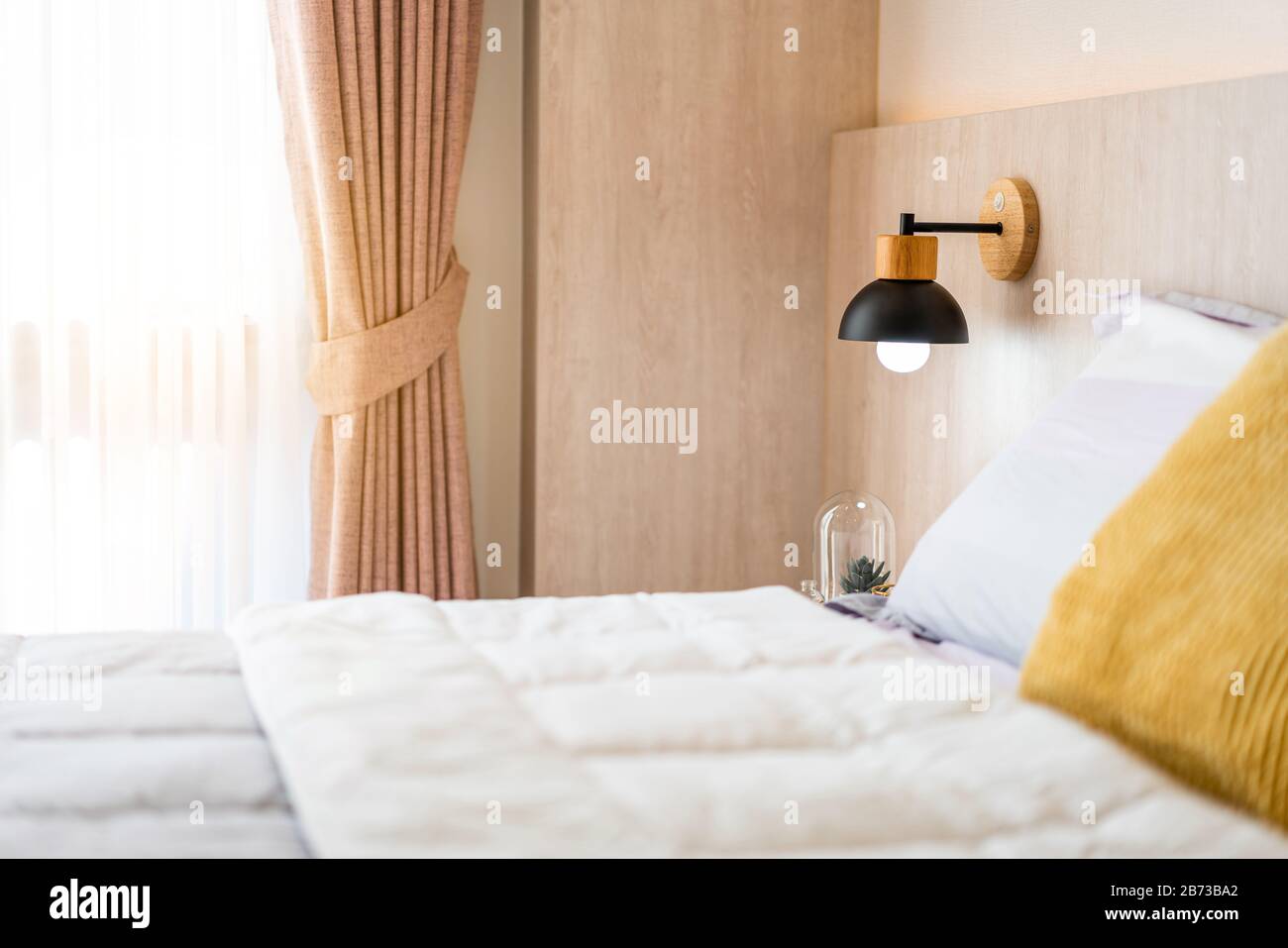 Stylish wooden, black color bedside lamp, wooden bed and grey blanket in the bedroom. Comfortable and elegant interior design for a cozy atmosphere. Stock Photo