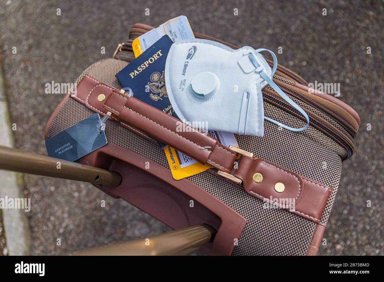 Boston, USA - March 13th 2020: Air traveler business baggage with face mask for protection against the sars-cov-2 virus. Stock Photo