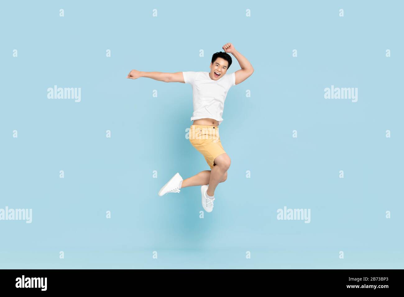 Happy handsome Asian young man in casual clothes smiling and jumping in light blue pastel background Stock Photo