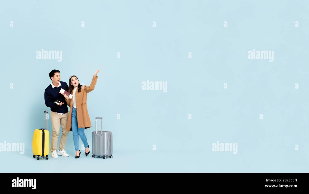 Lovely Asian couple tourists with baggage  about to go for winter honeymoon travel isolated on light blue background with copy space Stock Photo
