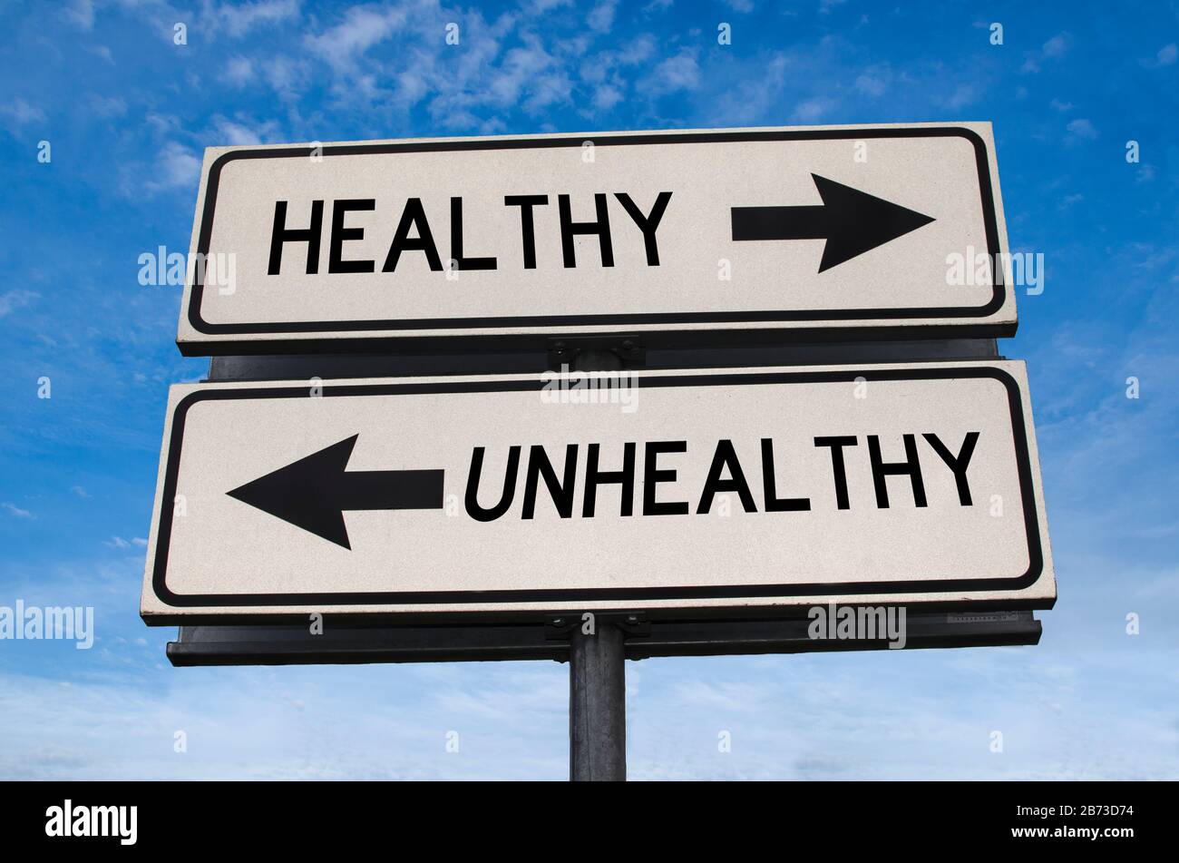 Unhealthy vs healthy. White two street signs with arrow on metal pole with word. Directional road. Crossroads Road Sign, Two Arrow. Blue background Stock Photo