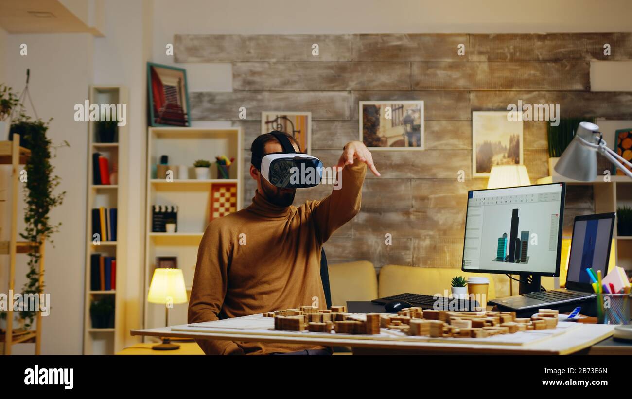 Young architect using virtual reality goggles modeling buildings in home office. Stock Photo