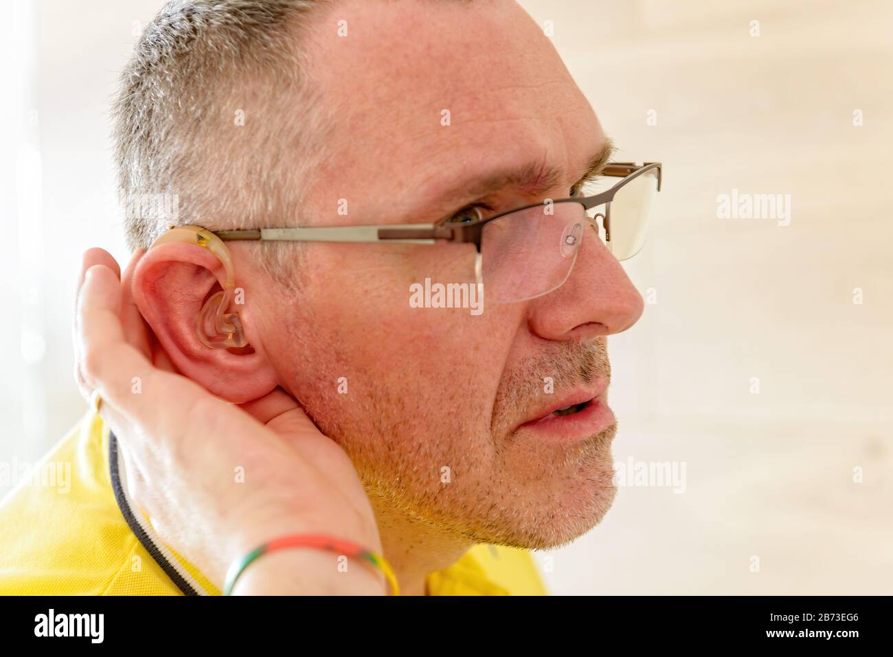Man wearing deaf aid in ear attempting to hear something Stock Photo