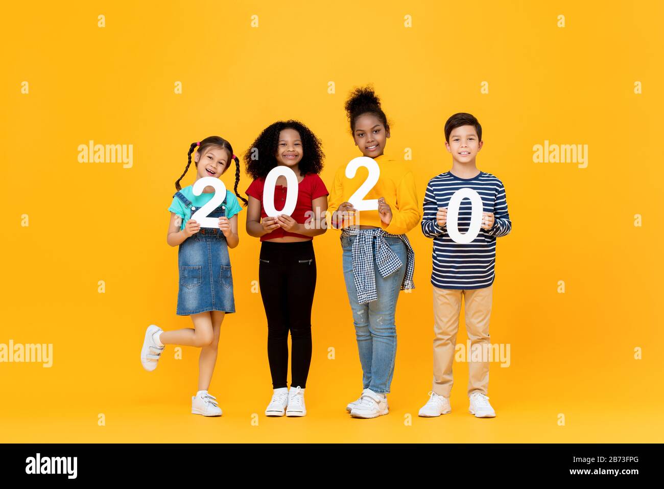 Cute mixed race kids smiling and holding 2020 numbers for new year concept isolated on yellow background Stock Photo