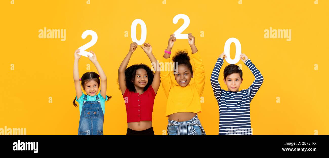 Cute mixed race kids smiling and holding 2020 numbers for new year concept isolated on yellow  banner background Stock Photo