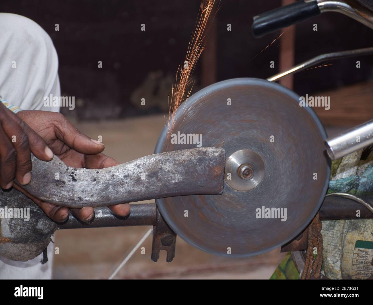 A big knife like object also called Bothi or Dao is sharpened by an indian man in his bicycle powered stone wheel Stock Photo