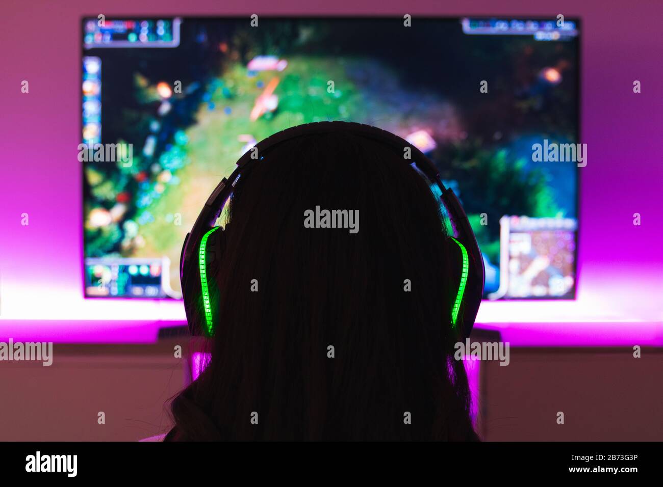 Stock photo of a gamer girl with headphones playing a video game in front of the tv Stock Photo