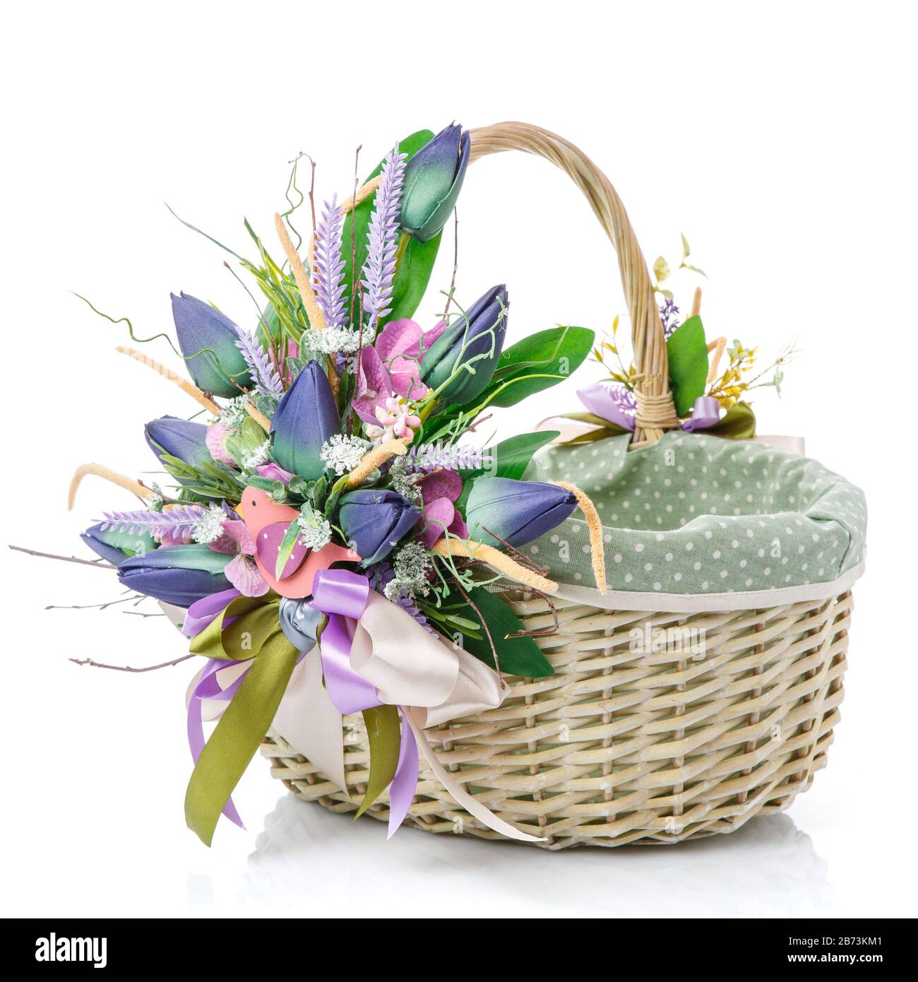 Easter basket with fabric inside on white background. Decorated with large decoration of blue tulips, greenery and decorative wooden bird. Stock Photo