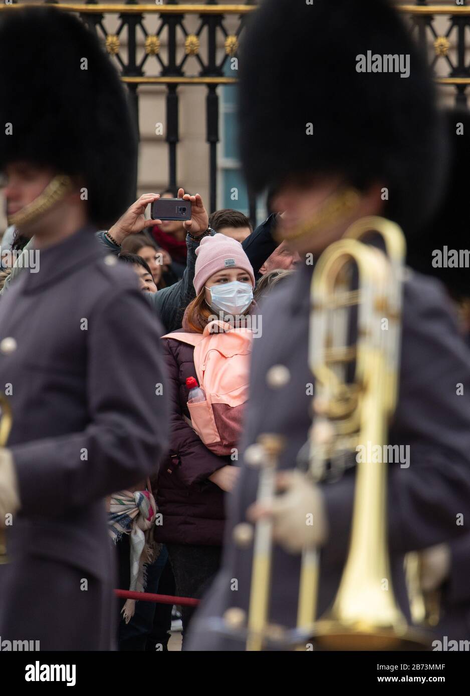 A woman wearing a protective face mask watches the Changing of the Guard ceremony outside Buckingham Palace, London, the day after the Prime Minister said that Covid-19 'is the worst public health crisis for a generation', and the government's top scientist warned that up to 10,000 people in the UK are already infected. PA Photo. Picture date: Friday March 13, 2020. See PA story HEALTH Coronavirus. Photo credit should read: Dominic Lipinski/PA Wire Stock Photo
