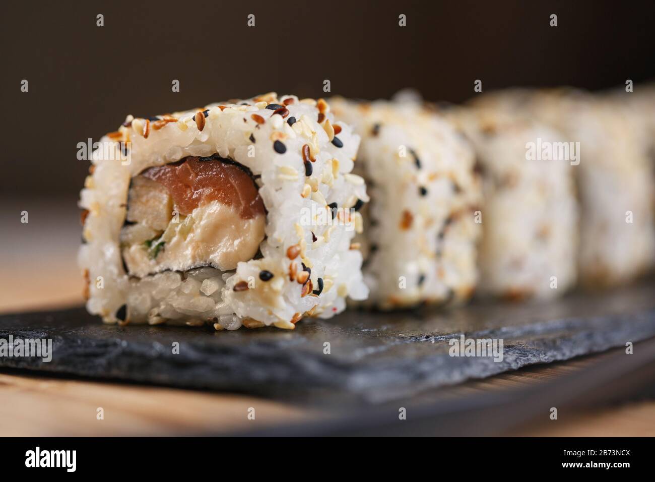 Sushi roll with salmon, eel, cucumber, cream cheese and sesame on a black board. Japanese food. Stock Photo