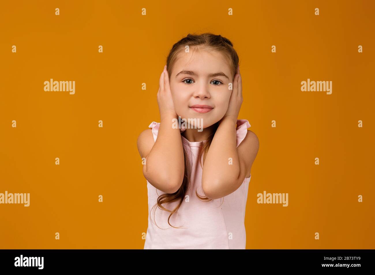Little child girl covering her ear with her hand. I hear nothing Stock