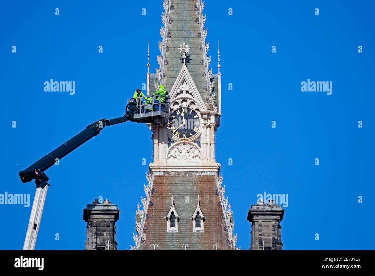 Fettes College Building, Edinburgh, Scotland, UK. 13th Mar 2020. Maintenance workers on the platform of an enormous crane, checks being carried out on the clock tower of the historic building by workers in hard hats and yellow jackets. This Public School famously was where Tony Blair was educated. The College was founded in 1870. It was designed by David Bryce, and completed (1864-70) in Scots Baronial style. Stock Photo