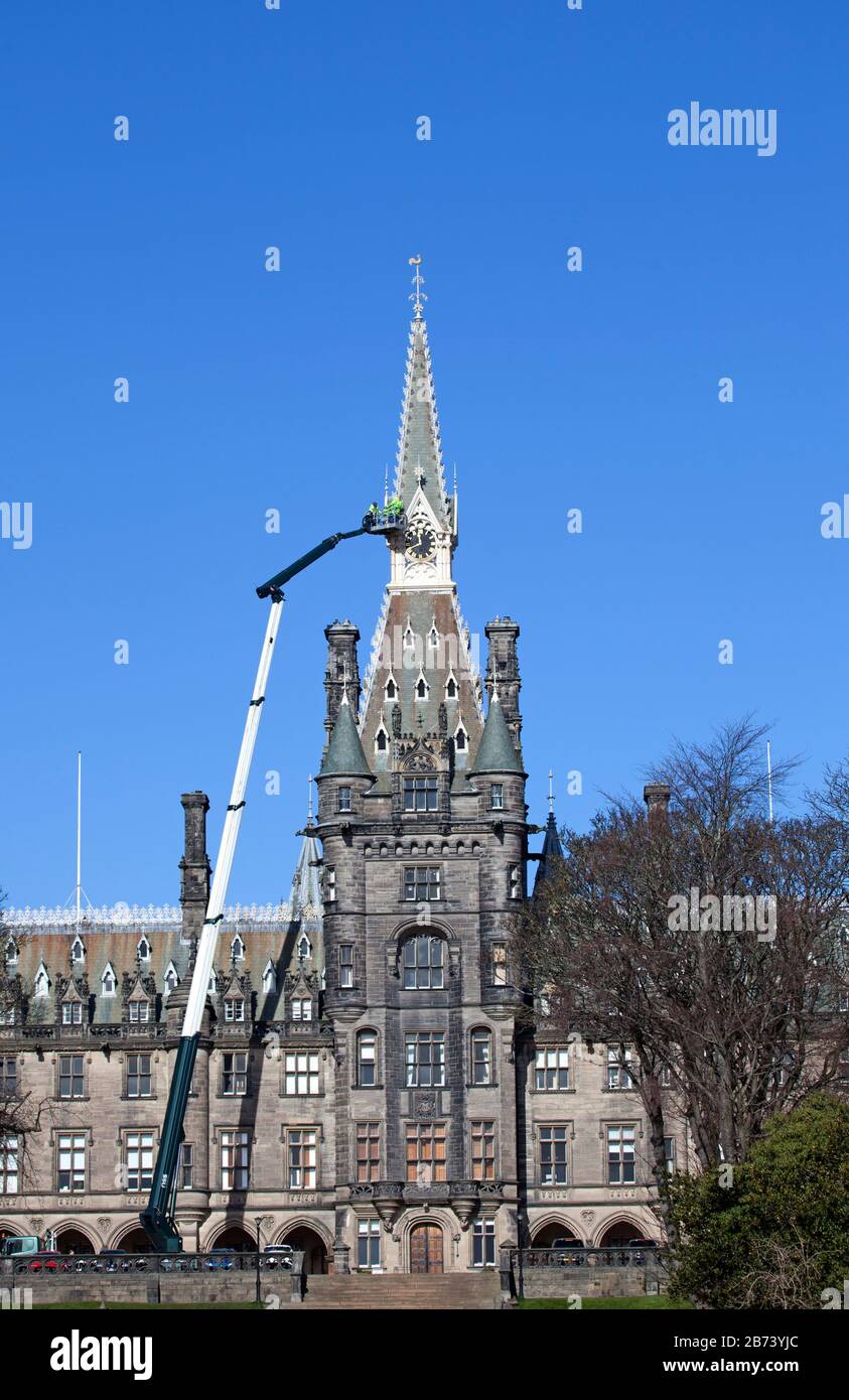 Fettes College Building, Edinburgh, Scotland, UK. 13th Mar 2020. Maintenance workers on the platform of an enormous crane checks being carried out on the clock tower of the historic building by workers in hard hats and yellow jackets. This Public School famously was where Tony Blair was educated. The College was founded in 1870. It was designed by David Bryce, and completed (1864-70) in Scots Baronial style. Stock Photo