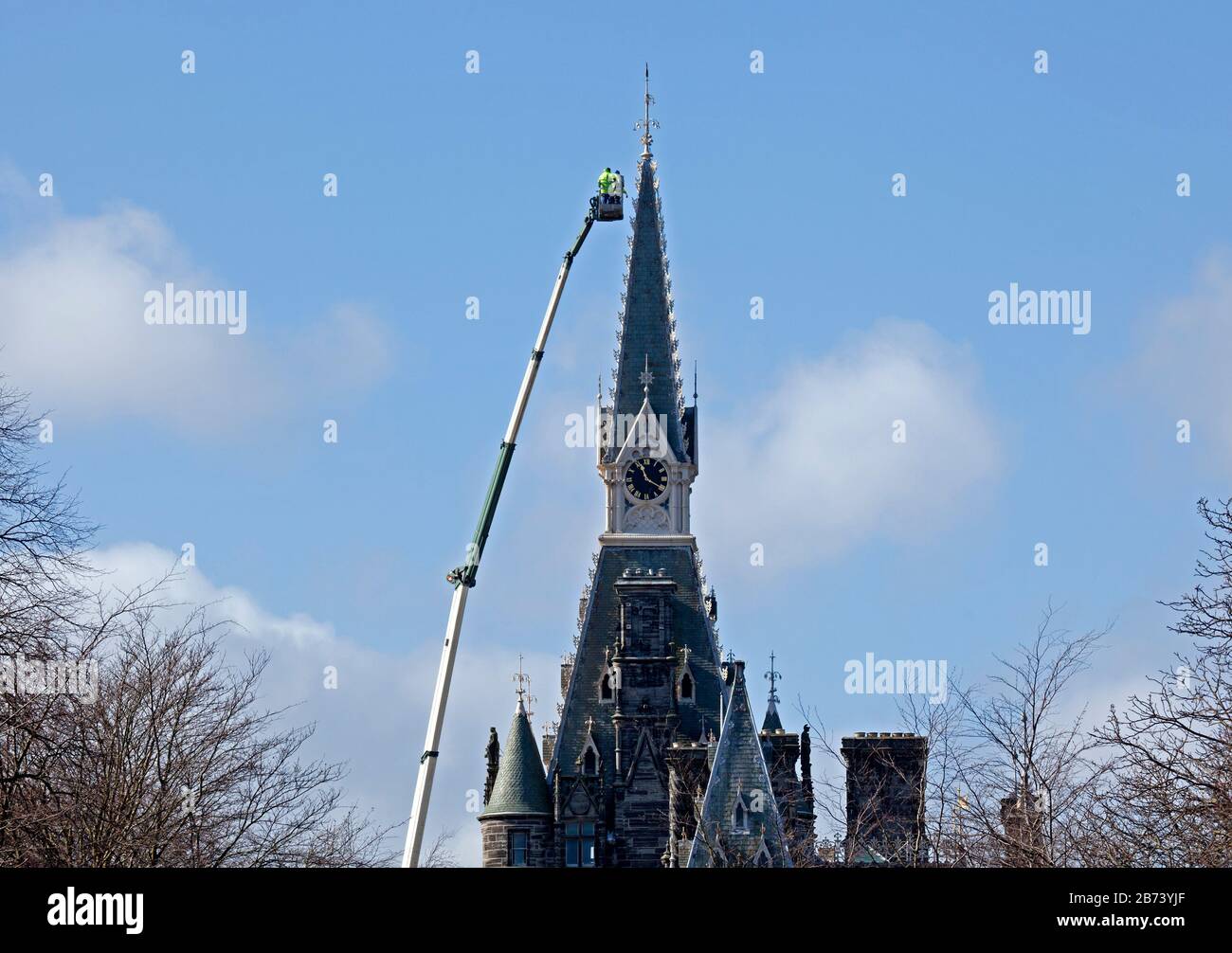 Fettes College Building, Edinburgh, Scotland, UK. 13th Mar 2020. Maintenance workers on the platform of an enormous crane, checks being carried out on the clock tower of the historic building by workers in hard hats and yellow jackets. This Public School famously was where Tony Blair was educated. The College was founded in 1870. It was designed by David Bryce, and completed (1864-70) in Scots Baronial style. Stock Photo