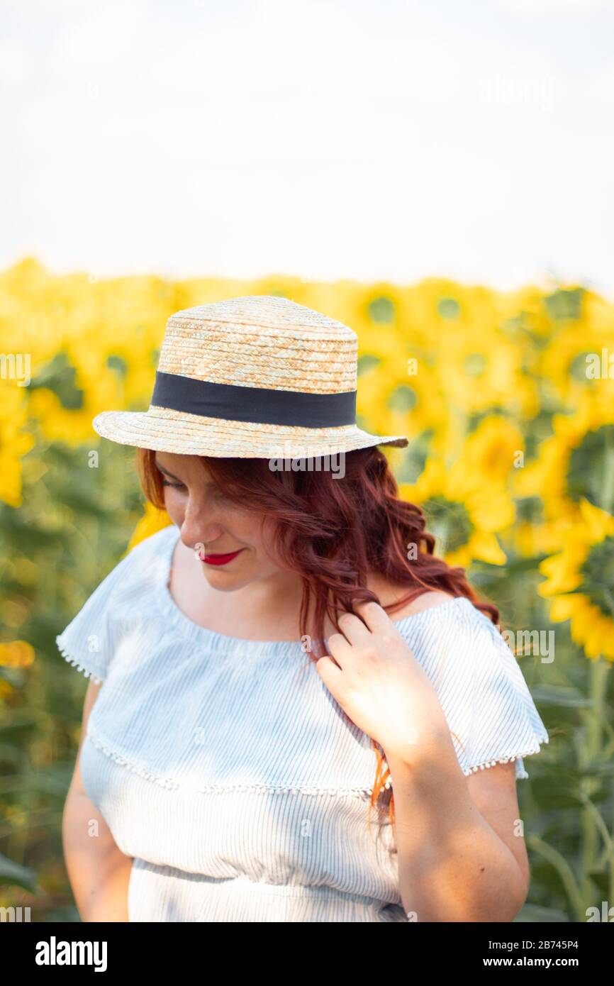 Young red hair Caucasian girl in straw hat and dress in sunflowers. Red ...