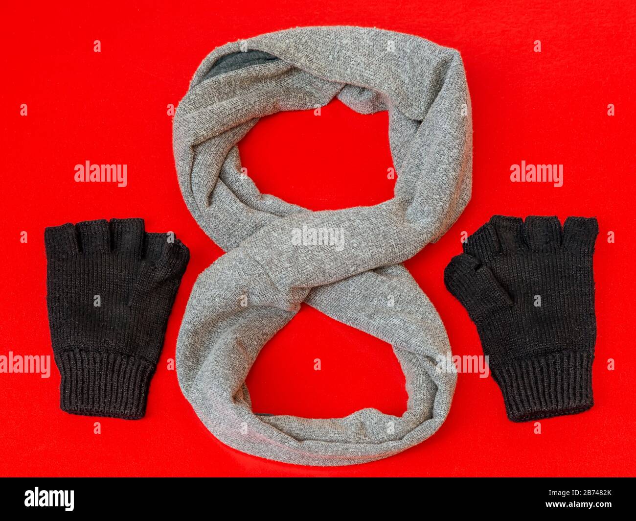 Composition of gray scarf and black gloves, both of wool, on a bright red background. Stock Photo