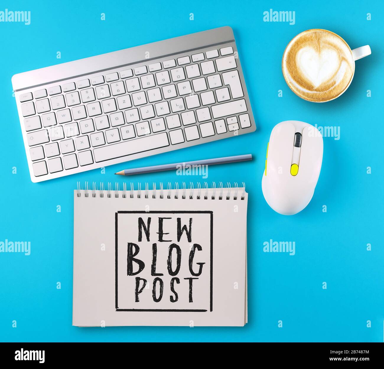 top view of text NEW BLOG POST written on spiral notepad on colorful desk with keyboard, computer mouse and coffee mug Stock Photo