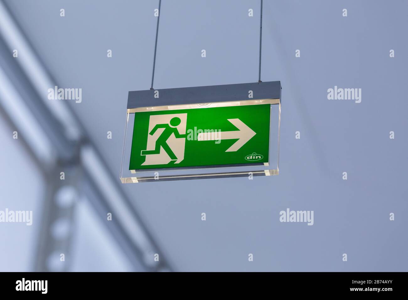 Close up of illuminated emergency exit sign (colored green and white). Modern design, with running figure and arrow to the right. Neutral, background. Stock Photo