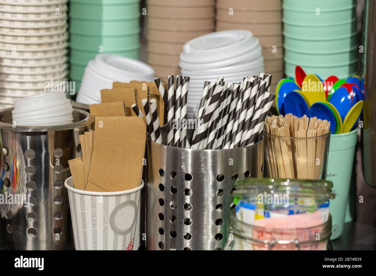 Want some coffee to go? The equipment you need is there: Striped drinking straws, coffee cups, lids, wooden sticks, plastic spoons. In a café. Stock Photo