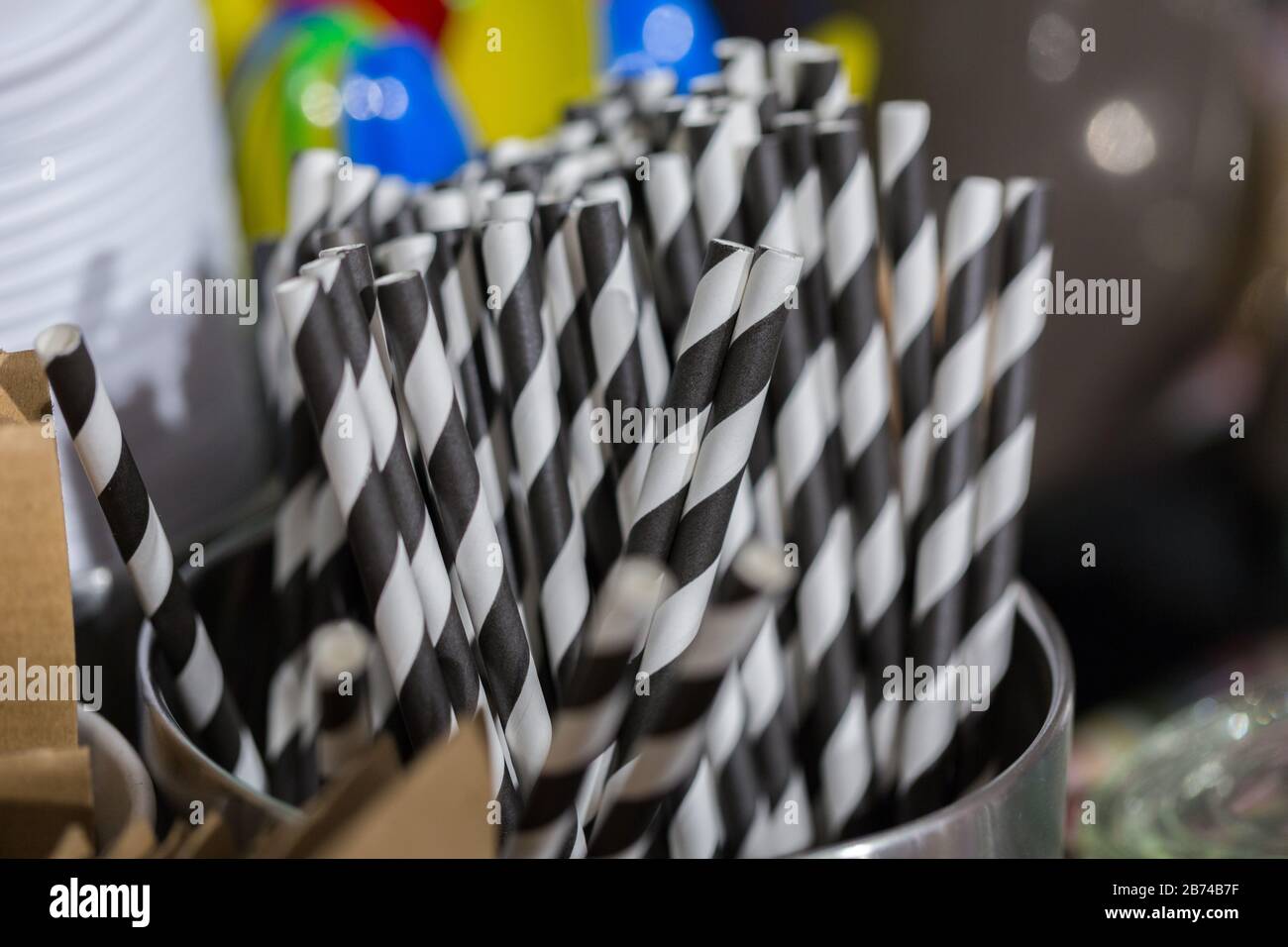 Close up of black & white striped drinking straws. Used for hot and cold beverages. In the background plastic spoons in different colors. Stock Photo