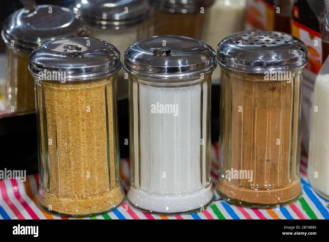 Three glass jars with metallic top filled with white sugar, brown sugar and cinnemon. For sweetening or giving a special taste to hot beverages. Stock Photo