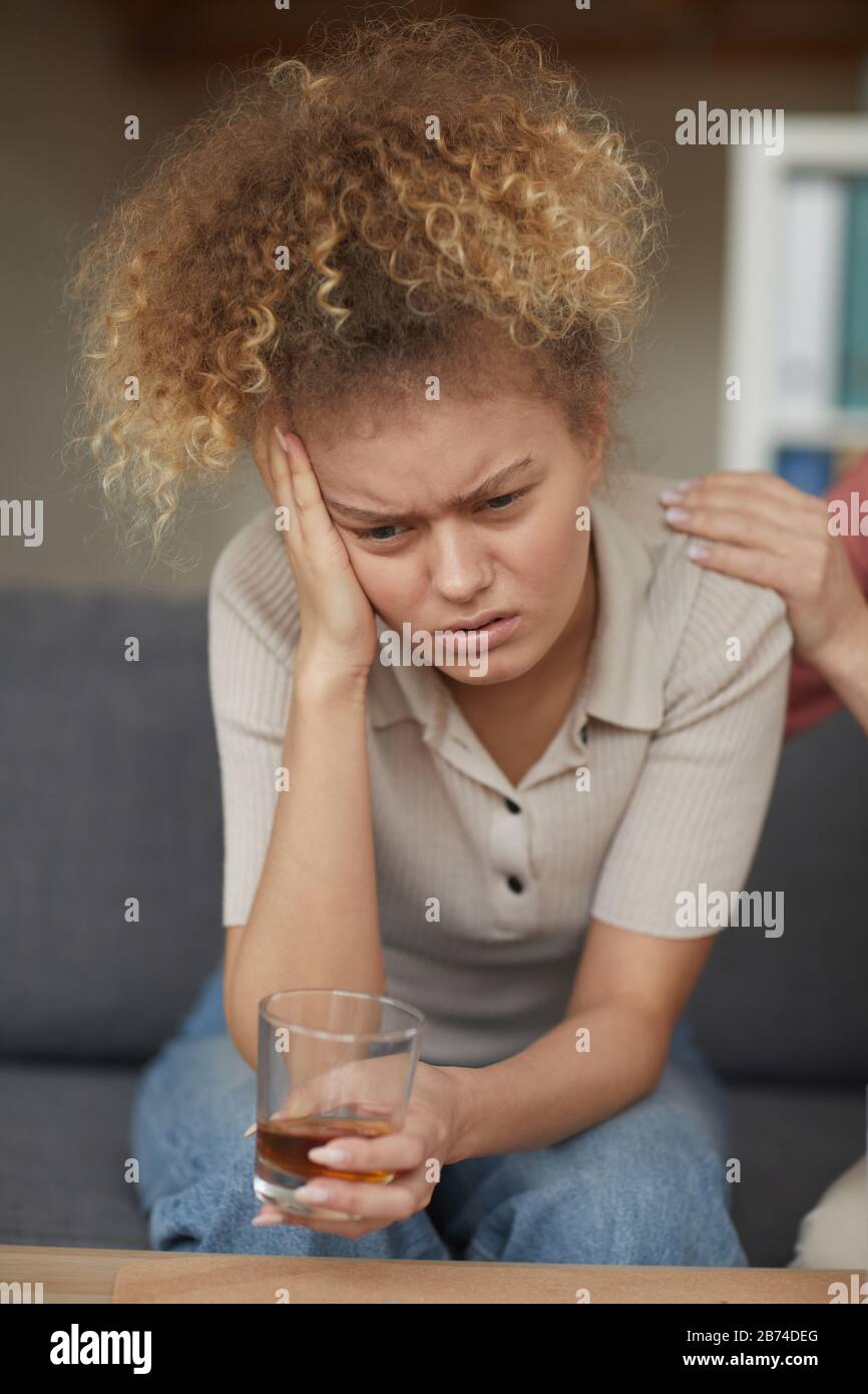 Young depressed woman sitting on sofa and drinking alcohol at home Stock Photo