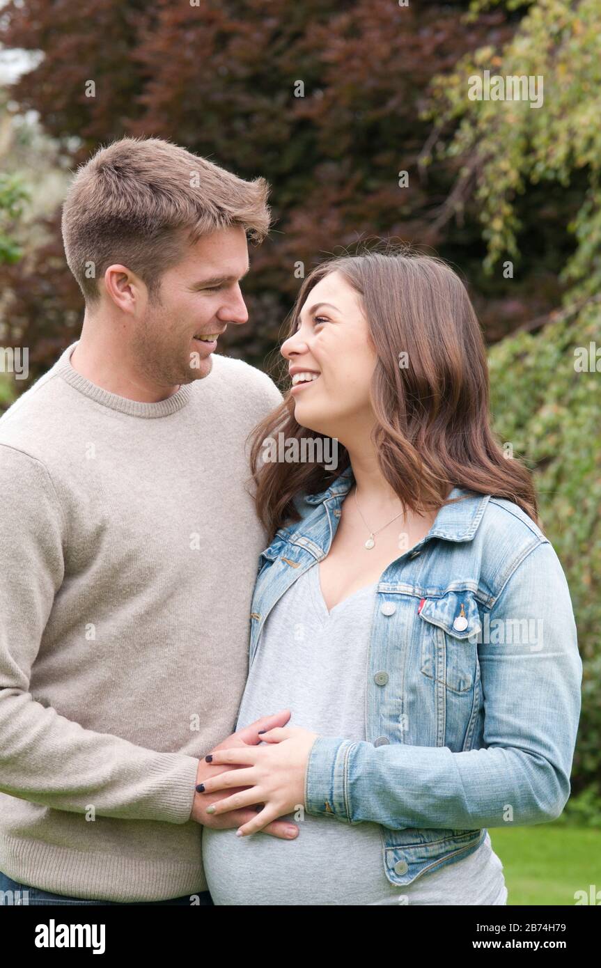 Pregnant young woman standing with her partner caressing her tummy Stock Photo