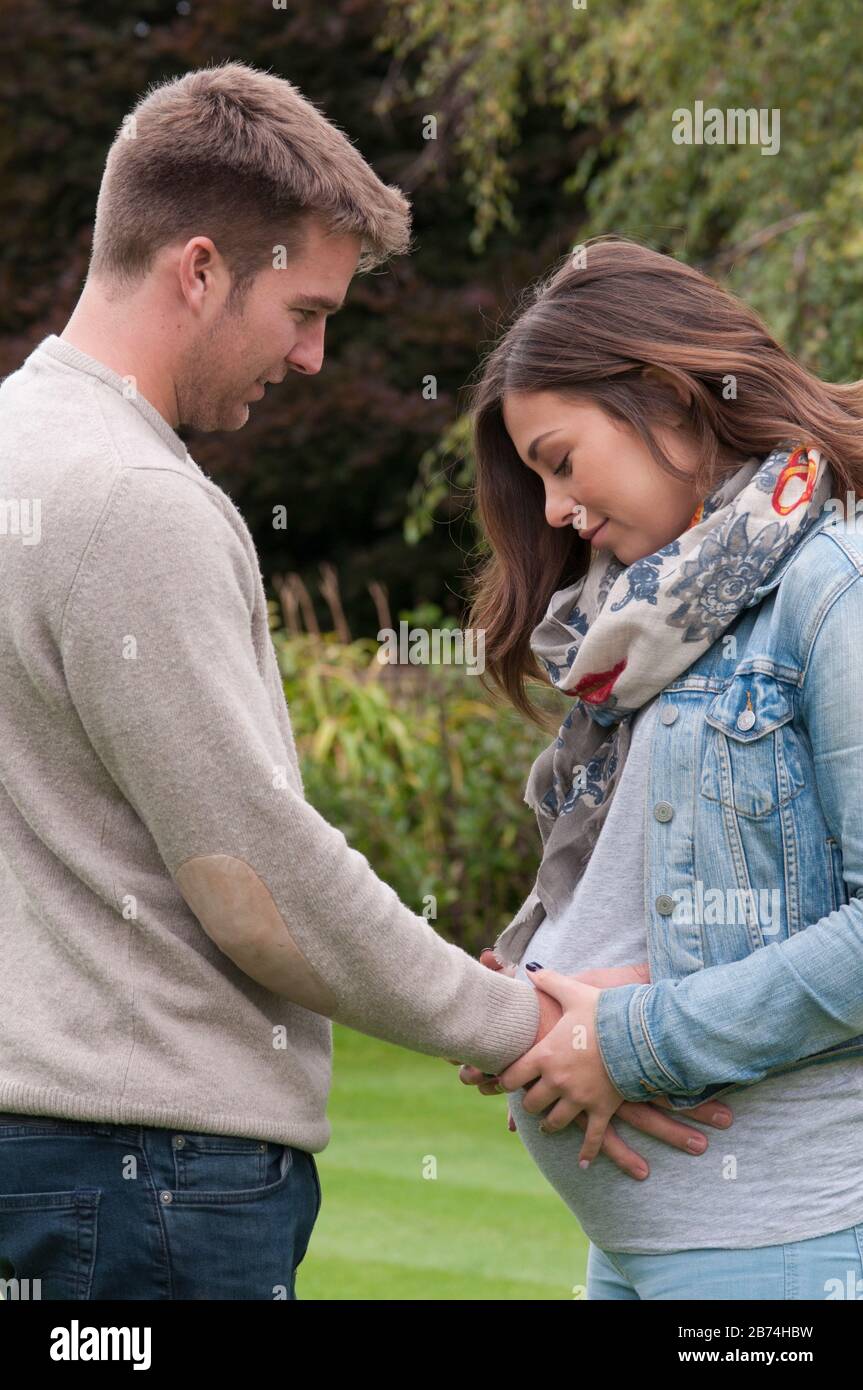 Young pregnant woman standing with her partner caressing her tummy Stock Photo