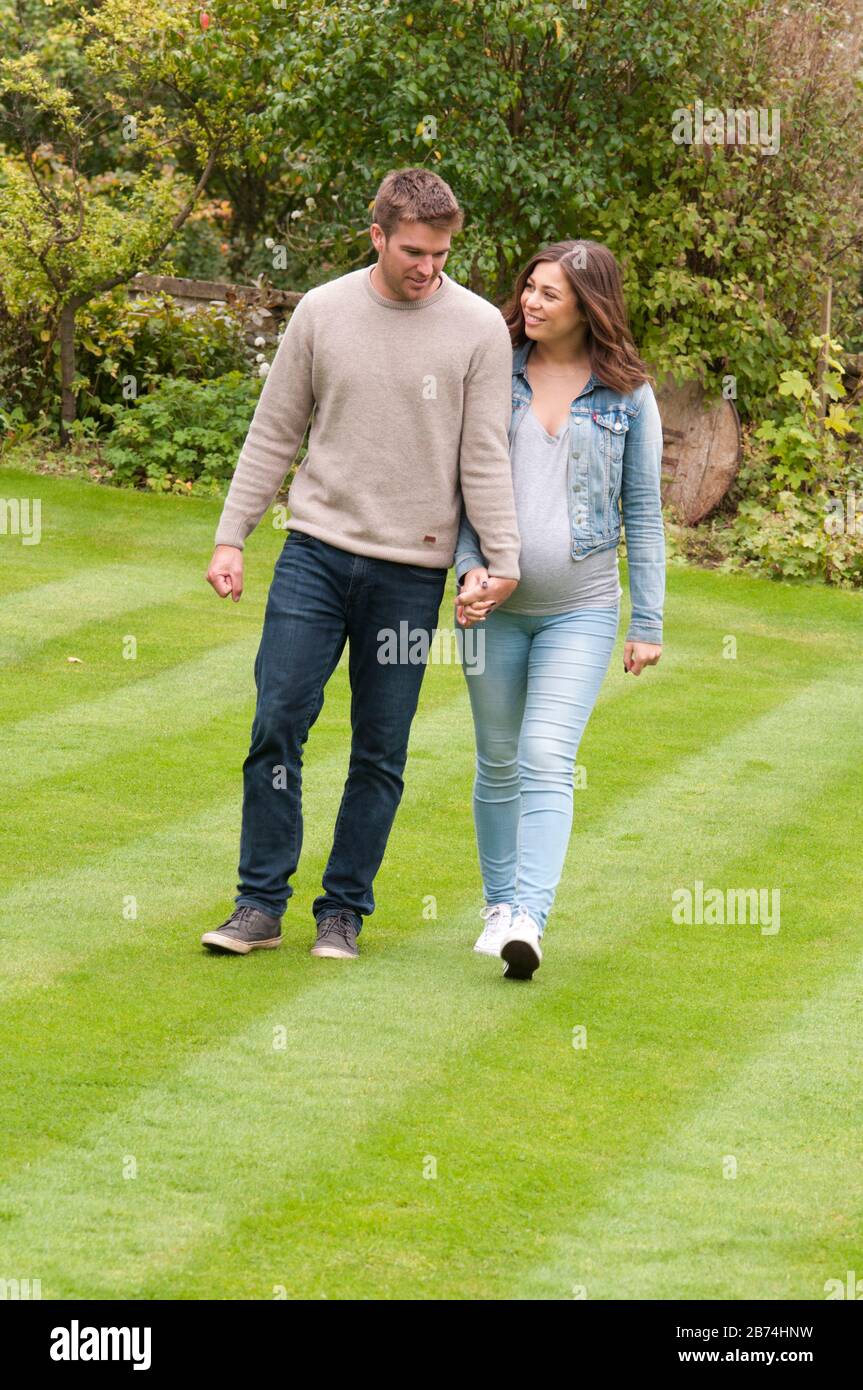 Pregnant young woman walking with her partner holding hands Stock Photo