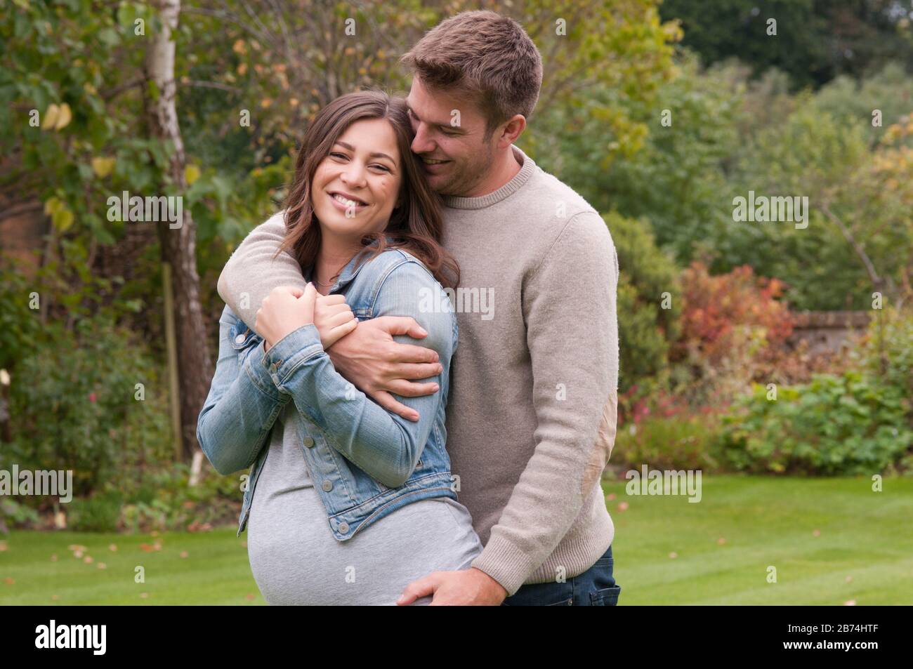 Beautiful pregnant young woman with her partner caressing her outside in their garden Stock Photo