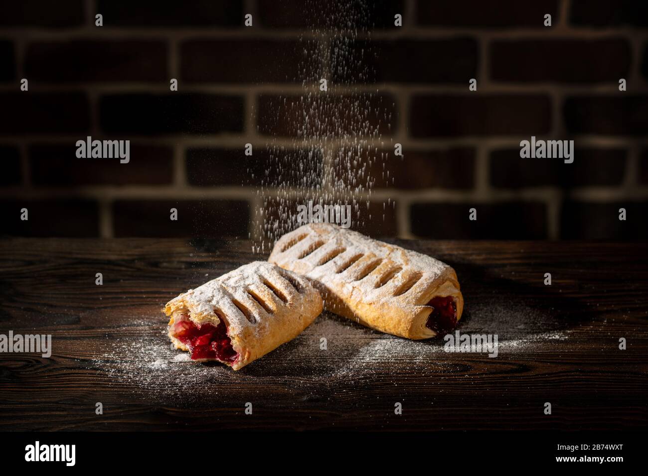 Strudel with cherries powdered with sugar on a wooden table and brick background Stock Photo