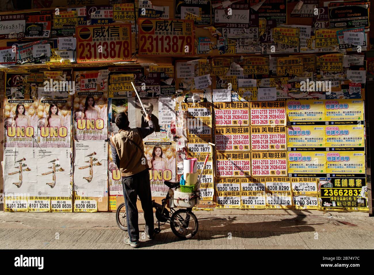 A worker stick a poster to the front of a closed shop in Tsim Sha Tsui of Hong Kong. Stock Photo