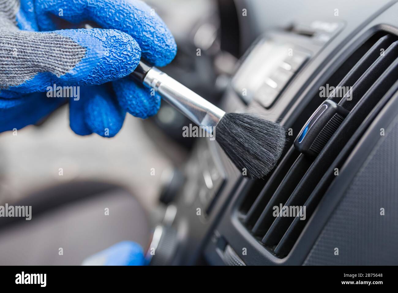 Worker cleaning automobile air conditioner vent grill with brush