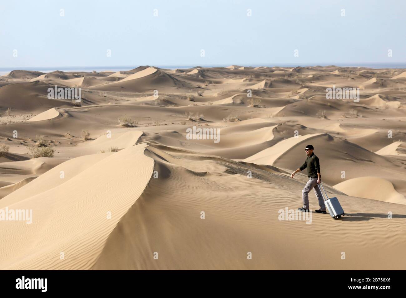 Symbolic image: Tourist with suitcase in the desert, Mesr Desert, Iran. The Mesr Desert is part of the central desert in Iran. [automated translation] Stock Photo