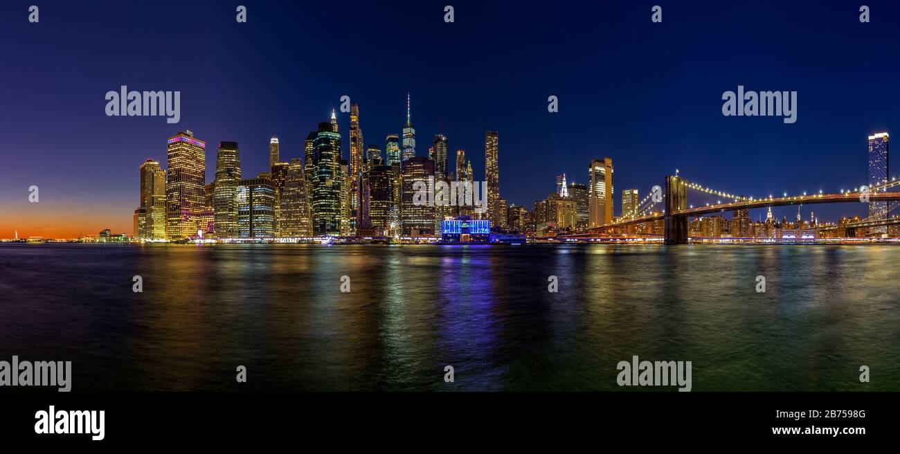 Panoramic image of lower Manhattan and the Brooklyn Bridge at night with the Hudson river reflecting the lights. Stock Photo