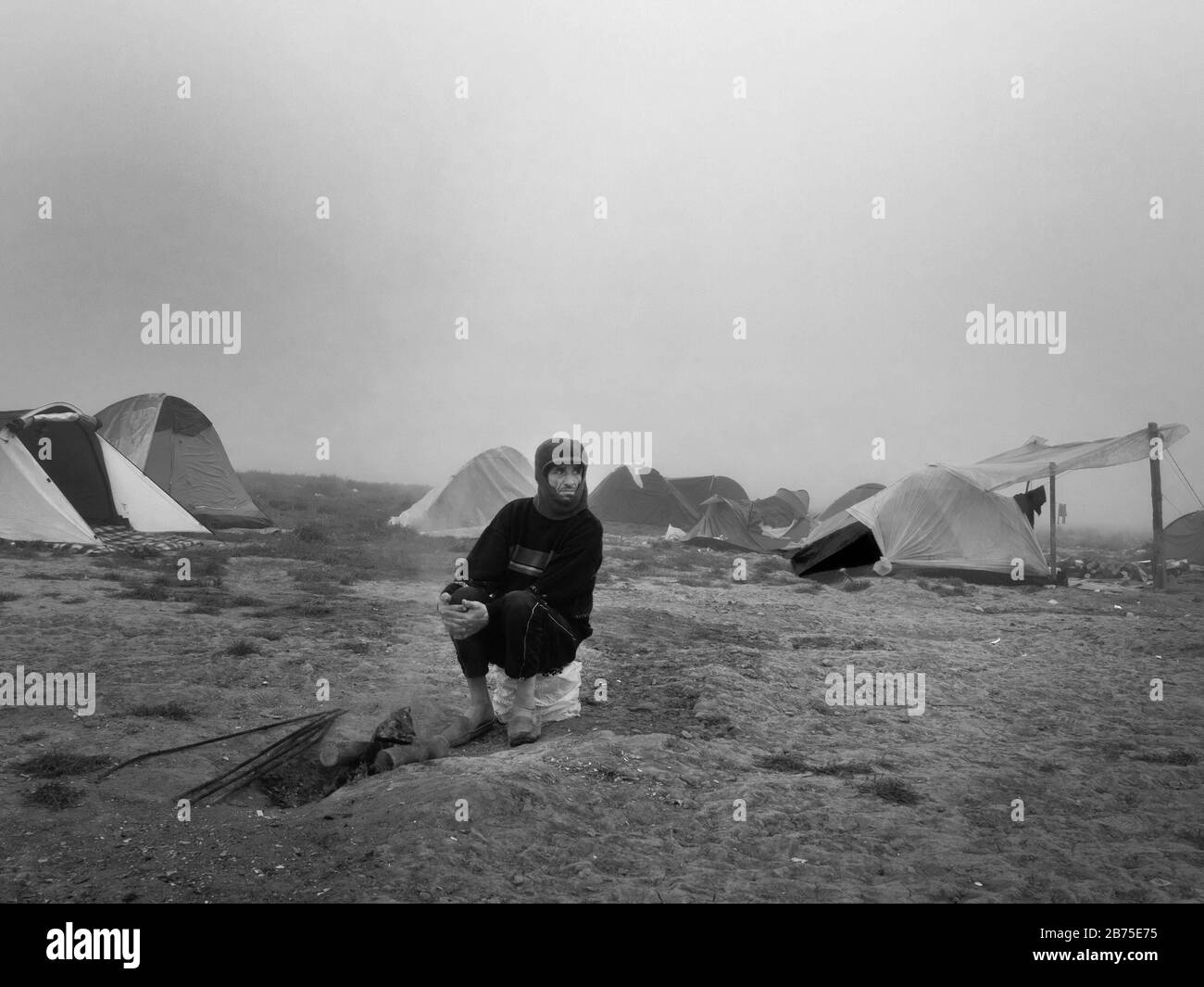 Refugee camp in Idomeni on the border with Macedonia. A man is sitting around a campfire at dawn. [automated translation] Stock Photo