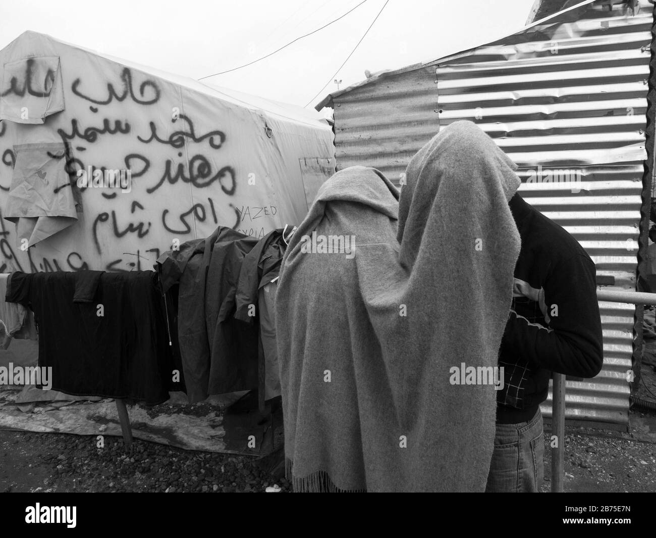 Refugee camp in Idomeni on the border with Macedonia. To protect themselves from the rain, two men hid under a blanket to talk on the phone. [automated translation] Stock Photo