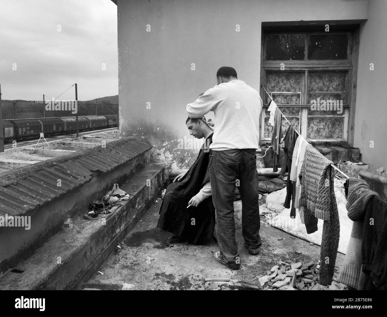 Refugee camp in Idomeni on the border with Macedonia. On a roof at the train station in Idomeni a hairdresser cuts a man's hair. [automated translation] Stock Photo