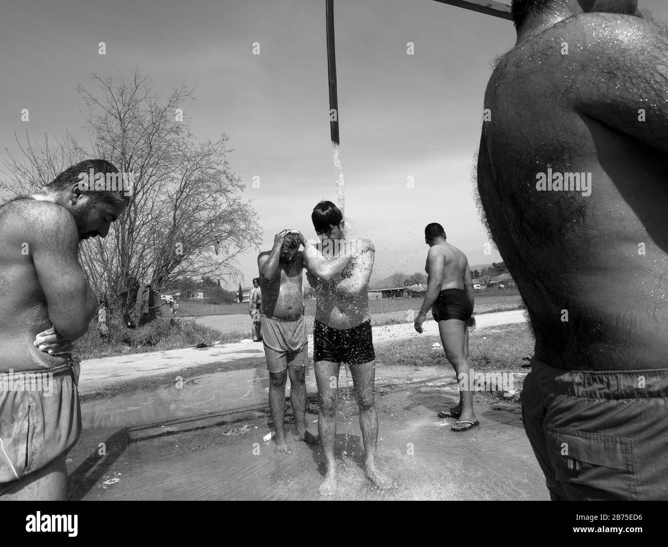 Refugee camp in Idomeni on the border with Macedonia. A group of men take a shower under a water tank of a local farmer. [automated translation] Stock Photo