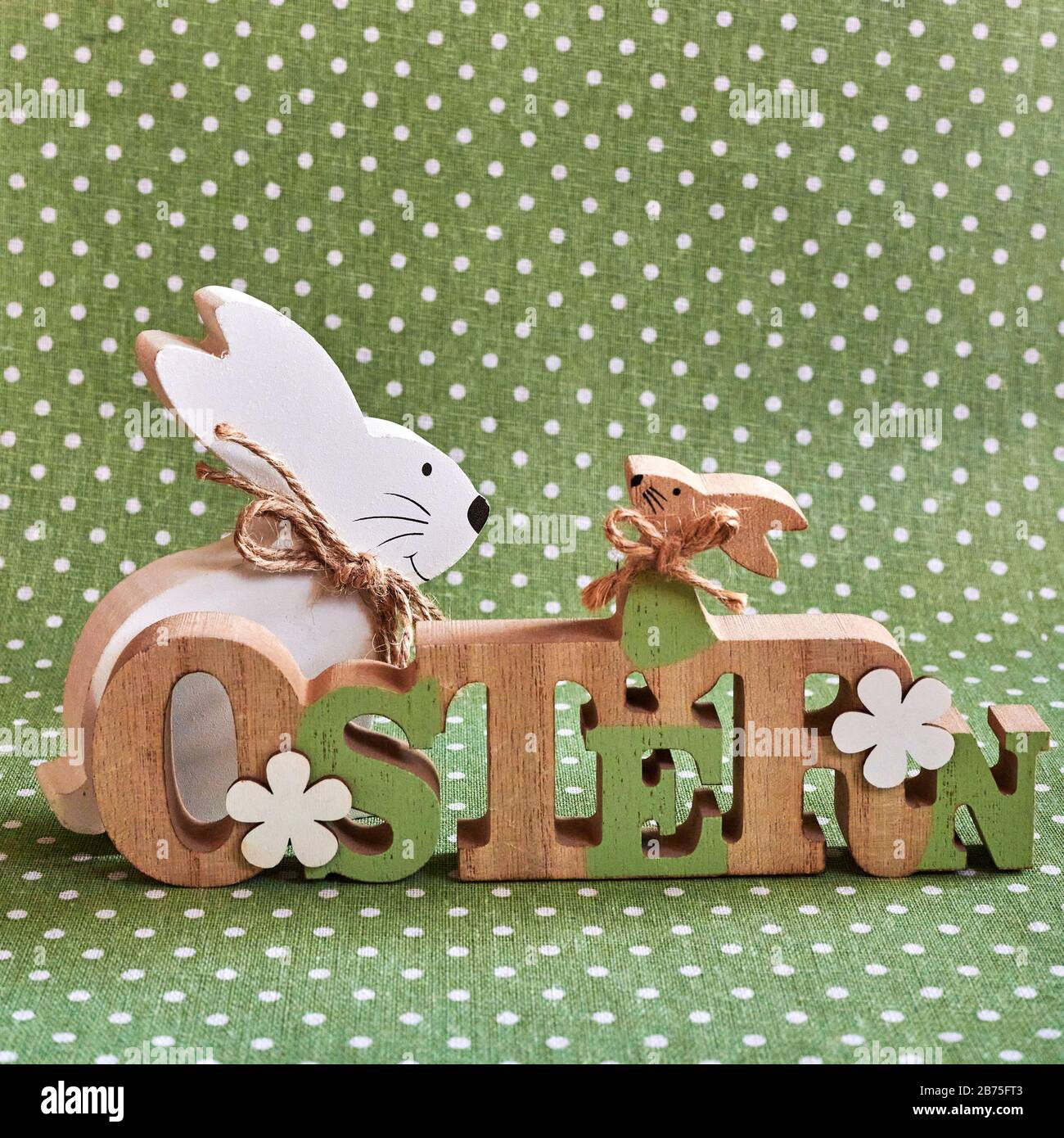 Wooden Easter bunny in front of a green background with white dots. The Text is German for Easter. Stock Photo