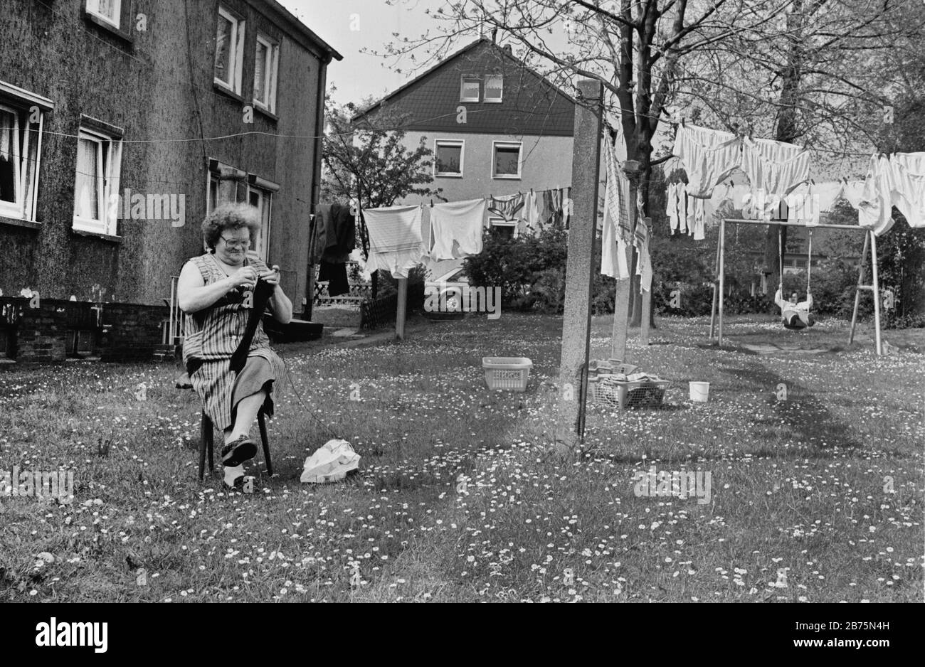 A woman is stuffing stockings in a backyard of a housing estate in Dortmund, laundry is hanging on washing lines and a child is swinging. June 19th, 1984. [automated translation] Stock Photo