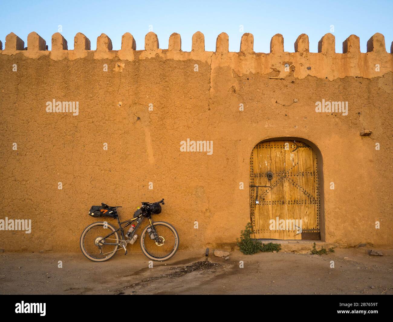 Bikepacking mountain bike leans against the earthen wall of a typical Berber adobe fortified house, a Tighremt, Agadir or Tiguemmi in Morocco. Stock Photo