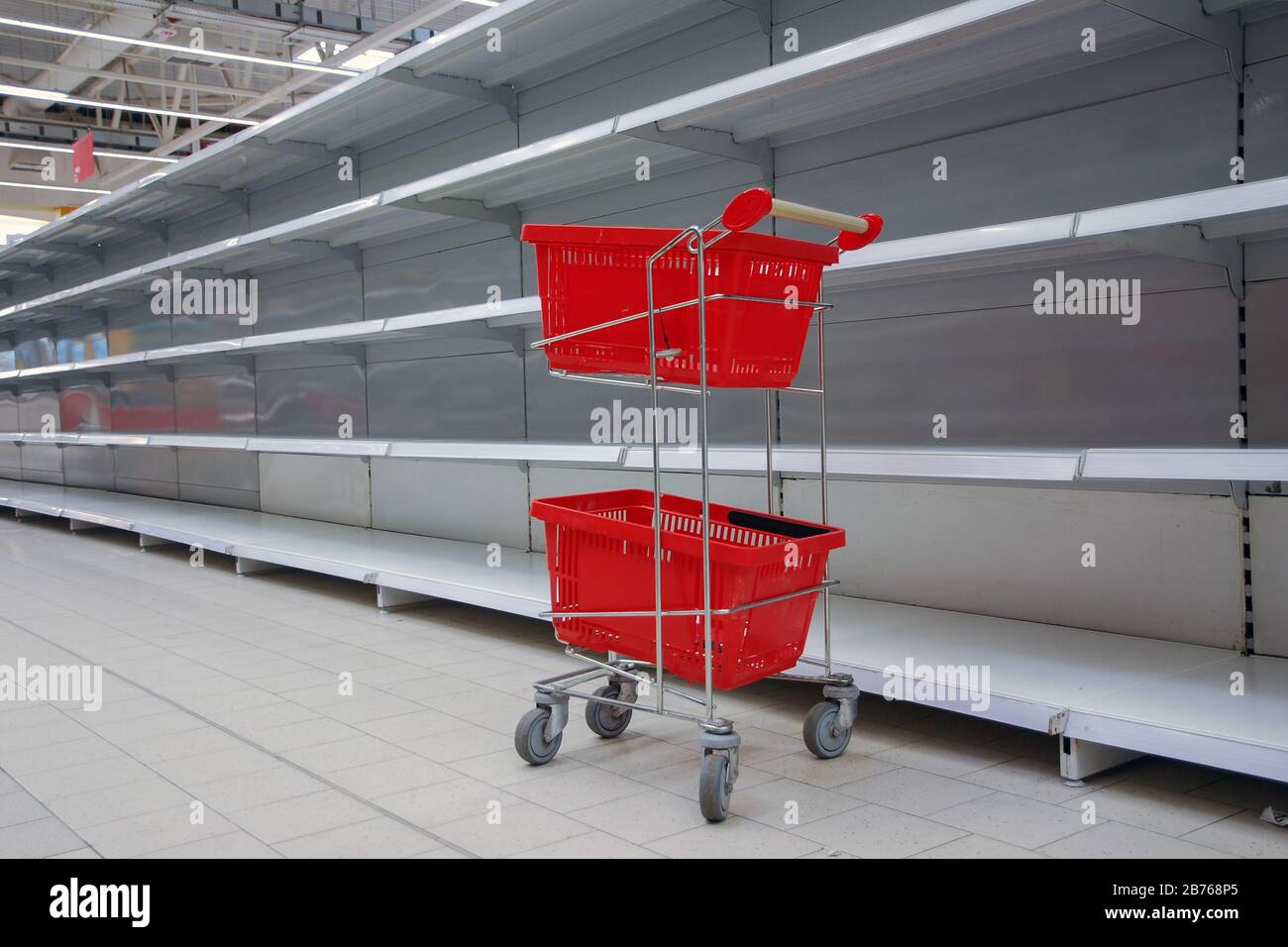 shopping trolley with empty baskets against empty shelves in grocery store Stock Photo