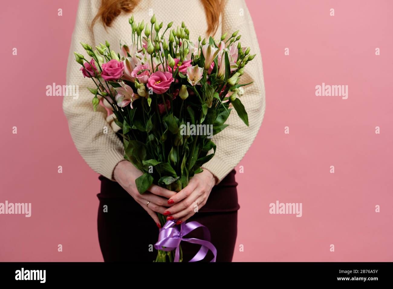 A tall bouquet of pink alstroemeria and eustomas in the hands of a red-haired girl standing on a pink background Stock Photo